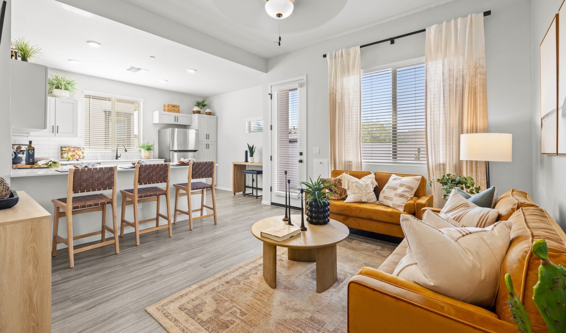 Bright and modern open-concept living area featuring a kitchen with white cabinets and stainless steel appliances, a large countertop with bar seating, and a cozy living room with mustard yellow sofas and stylish decor