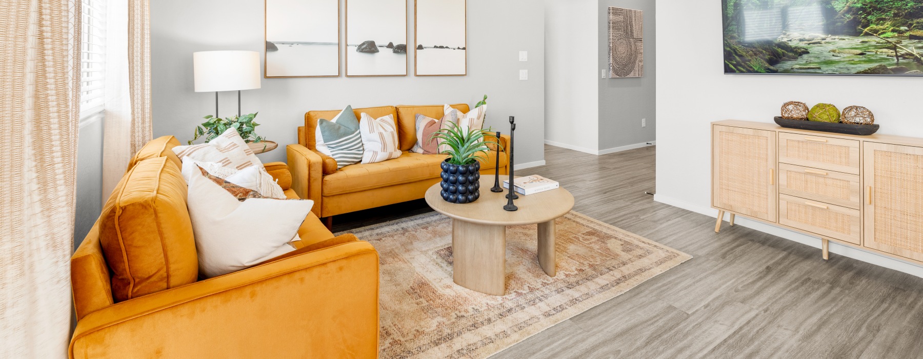 Cozy living room with mustard yellow sofas, a wooden coffee table, decorative pillows, and a rattan console cabinet beneath a wall-mounted TV