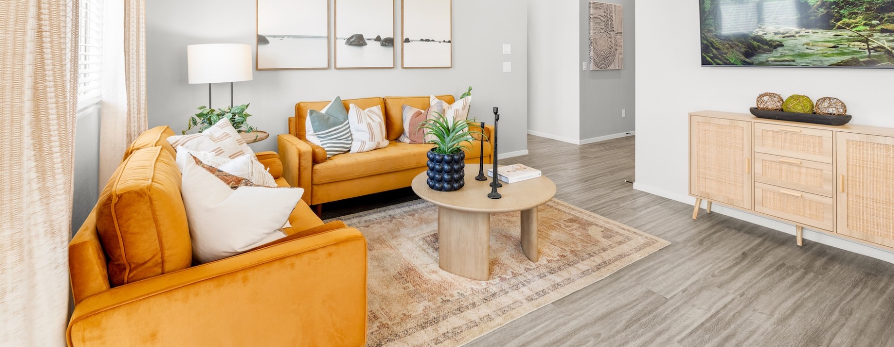 Cozy living room with mustard yellow sofas, a wooden coffee table, decorative pillows, and a rattan console cabinet beneath a wall-mounted TV