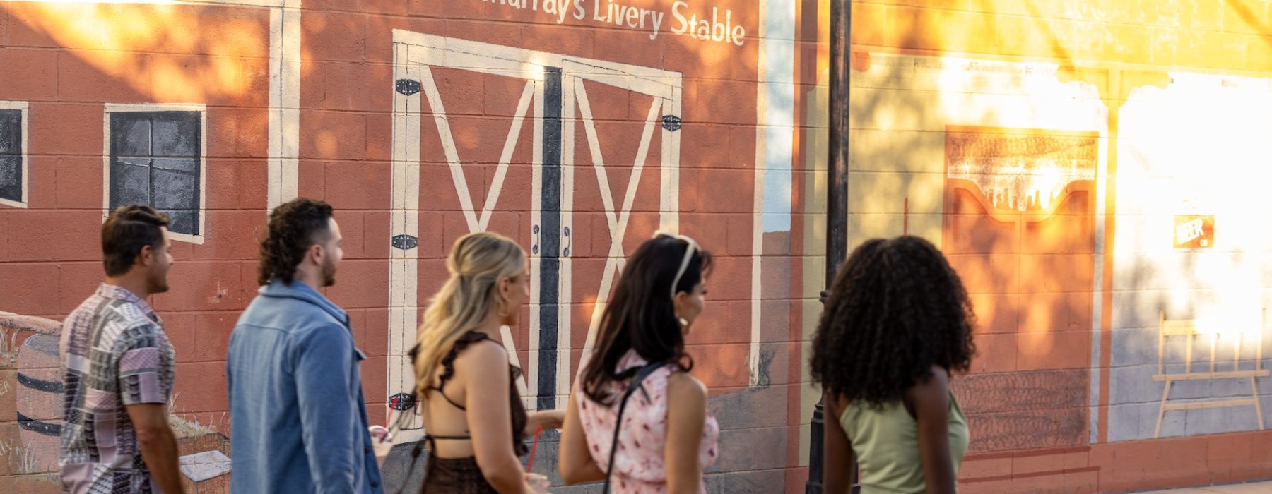 Group of friends walking through historic downtown Casa Grande, passing by a building with rustic red walls and barn-style doors